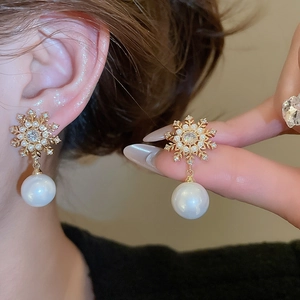Close-up of golden snowflake earrings with sparkling zircon and round white pearl drop
