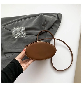 Detail view of a small brown oval leather crossbody bag with a slim strap and clasp