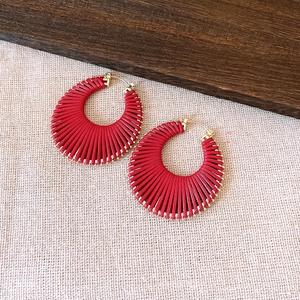 Bohemian style red woven hoop earrings with golden clasp on rustic background