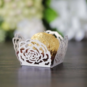 Detail of laser-cut white paper cupcake wrappers with rose patterns for wedding decor