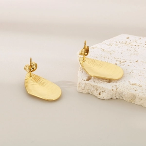 Detailed macro view of gold-plated stainless steel stud earrings with a brushed metal texture