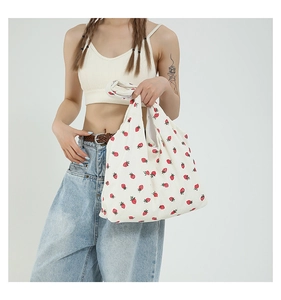 Dettaglio della borsa tote in tela crema con stampe di fragole rosse e tracolla larga