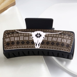 Detail of black hair claw clip featuring a brown Aztec pattern with a white bull skull motif