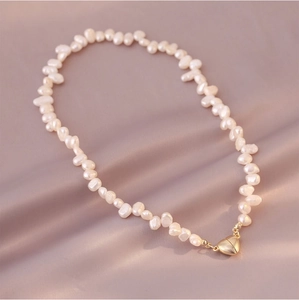 Detail of irregular white pearl necklace with a golden heart-shaped magnetic clasp