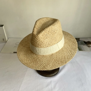 Detailed close-up of natural raffia straw hat texture with ivory white ribbon on wood stand