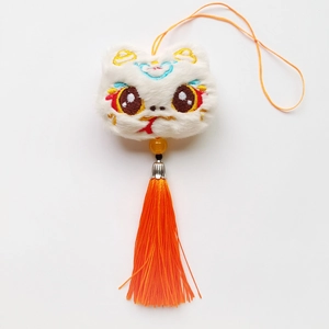 Détail d'un pendentif lion en peluche blanche avec broderies et long gland orange