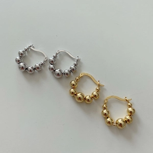 Close-up of gold and silver S925 beaded hoop earrings on a clean white surface