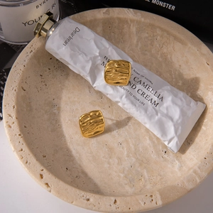 Detailed close-up of gold square earrings with hammered texture on a marble display tray