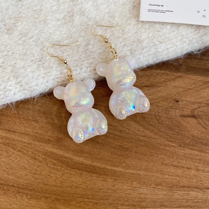 Detailed shot of iridescent white resin bear earrings on a rustic wood and fur surface