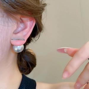 Close-up of a silver needle bar earring with sparkling pavé stones and a large grey pearl