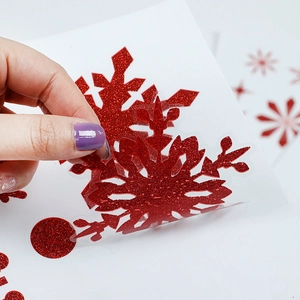 Close-up of hand peeling a red glitter snowflake static sticker from the white backing