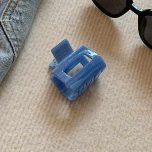Detail view of square blue marble cellulose acetate hair claw clip on beige fabric