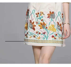 Detail of colorful floral embroidery and geometric border on a beige cotton dress hem