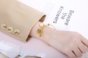 Detail of adjustable gold beaded bracelet featuring a heart love charm on a model's wrist
