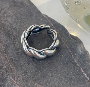 Macro detail of 925 sterling silver braided ring on a textured dark stone surface