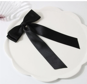 Detailed view of a black double-layered satin ribbon bow hair clip on a white decorative plate