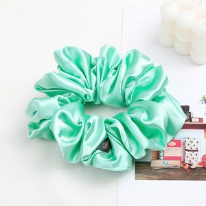 Detail of mint green satin hair scrunchie with rich folds and elegant brand label