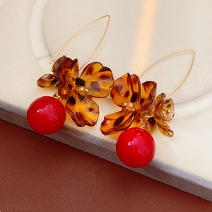 Close-up of leopard flower earrings with amber petals and glossy red spherical pendant
