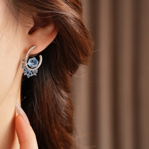 Close-up of U-shaped silver earring with blue hexagonal zircon stone on a model ear