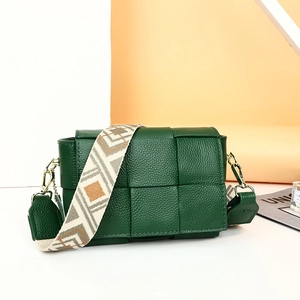 Detail of dark green woven leather bag with textured lychee grain and wide woven strap