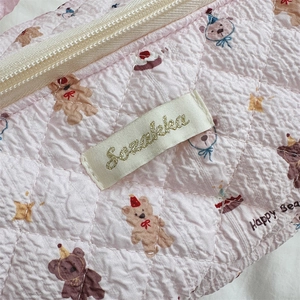 Detailed close-up of pink quilted cotton fabric with cute bear and cake embroidery