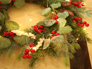 Detail of Christmas wreath with eucalyptus, red berries, pine cones and warm LED lights