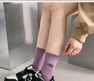 Detail of purple ribbed crew sock with circular VAMZONE logo embroidery and sneakers