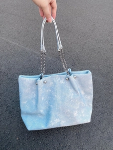 Ice blue denim tote bag with silver chain strap and metal rivets on asphalt background