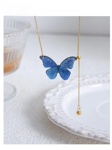 Makroaufnahme der Goldhalskette mit blauem Glitzer-Schmetterlingsanhänger auf Keramik
