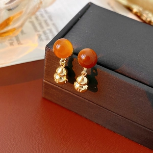 Macro shot of gold gourd earring with orange bead pendant on premium jewelry box edge