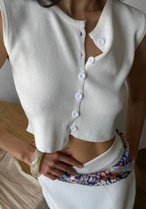 Close-up of white knitted sleeveless crop vest with button detail and soft texture