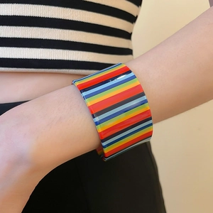 Detailed view of wide acrylic rainbow striped cuff bracelet on a female wrist