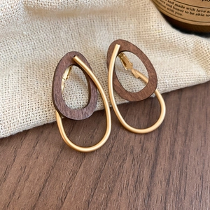 Détail des boucles d'oreilles gouttes en bois et métal doré sur fond de lin naturel