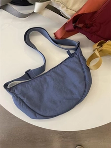 Detail view of a blue nylon crescent bag with adjustable strap on a white table
