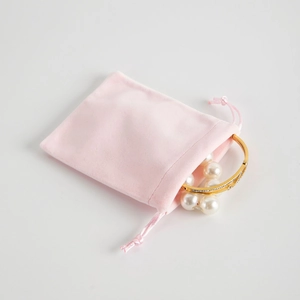 Pink velvet drawstring jewelry pouch with golden bracelet and pearl strand display