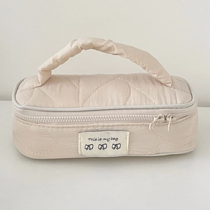 Close-up of beige quilted makeup bag featuring This is my bag label and bow patterns