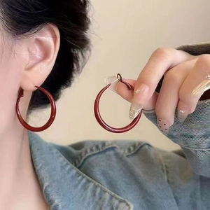 Close-up of model wearing large red resin hoop earrings with smooth glossy finish