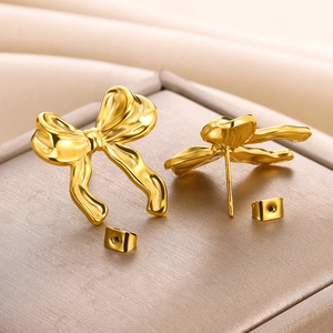 Detailed close-up of 18K gold-plated bow stud earrings on a brown jewelry box texture