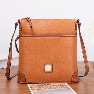 Detail of tan pebble leather crossbody bag with metal zippers on a rustic wooden desk