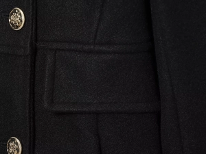 Detail of a black wool blend short coat showing gold buttons and a flap pocket