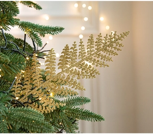 Detail of golden glitter fern leaf nestled in dark green Christmas tree branches