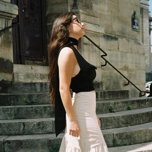 Side view of a woman wearing a black tie-up halter top and a ruffled cream maxi skirt