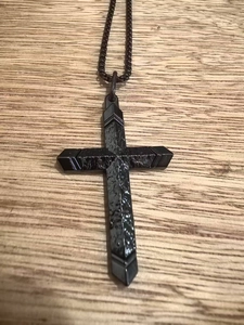 Détail macro du collier croix en acier inoxydable noir avec texture martelée sur bois