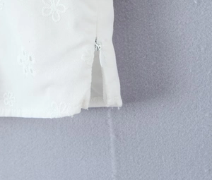 Detail view of white v-neck top featuring floral embroidery and a hidden side zipper