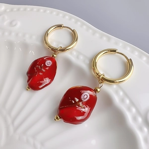 Detailed close-up of water ripple gold earrings with red glass charms on ceramic plate
