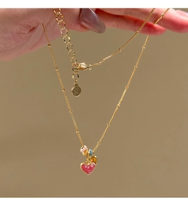 Macro view of gold plated heart pendant with pink enamel and colorful beads detailing