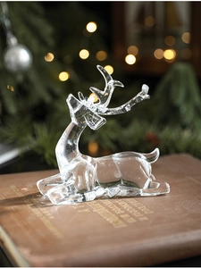 Detail of transparent acrylic reindeer ornament on vintage book with warm bokeh lights