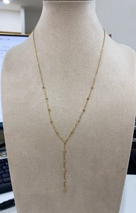 Detail of a gold Y-shaped titanium steel necklace with a cross pendant on a beige mannequin