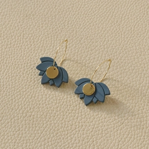 Detailed close-up of blue lotus-shaped earrings with gold metal centers on beige leather