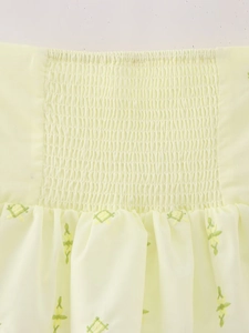 Détail de la taille smockée avec broderie florale verte sur une blouse en mousseline